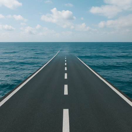 The asphalt road goes into the endless ocean under the blue sky. Space for textの素材