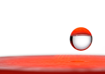A drop of water in the air above a red surface. Space for textの素材