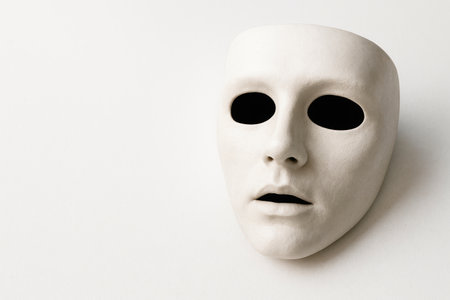 A white mask with empty eye sockets on a light background. Space for textの素材