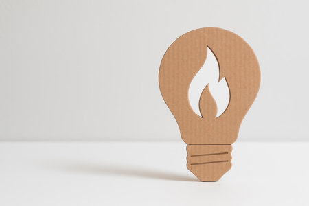 A cardboard light bulb with a flame cut out on a light background. Space for textの素材