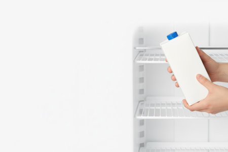 The hand puts a white carton of milk in the refrigerator. Space for textの素材