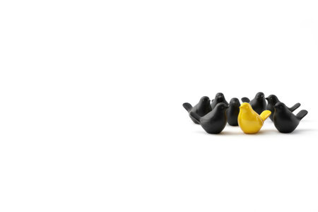 A yellow bird among black bird figurines as a symbol of individuality. Space for textの素材
