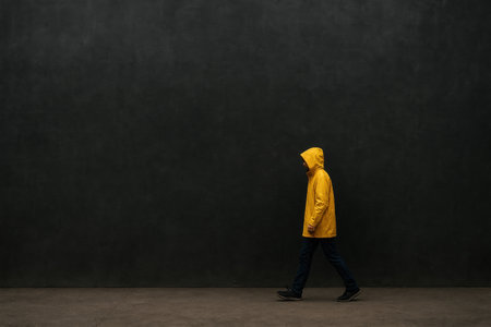 A man in a yellow cloak walks along a dark wall. Space for textの素材