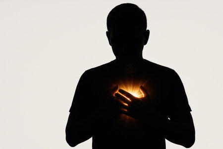 Silhouette of a man with a shining light in the heart area. Space for textの素材