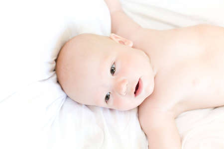 Funny little baby on white bed. View from above