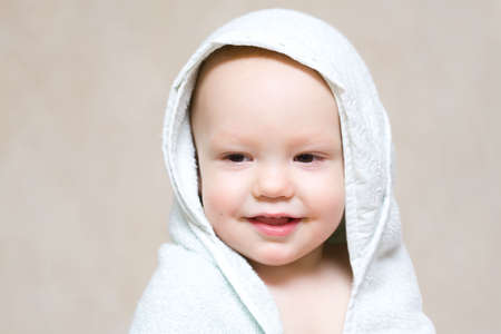Little happy baby under light blue towel after bath over gray backgroundの写真素材