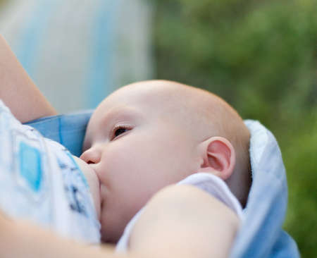Mother breast feeding her infant in sling (strap of cloth used to carry baby under 2 years)