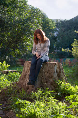 Young sad melancholic woman sit on big stub at sunlight dayの写真素材