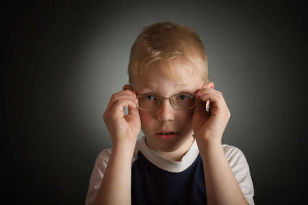 Boy try on a glasses. Over grey background with light spot centerの写真素材