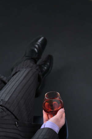 Businessman in formal dress relax with glass of cognac over black background. Image with copyspace. Focus on glass.の写真素材