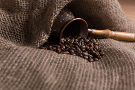 Cezve with freshly roasted coffee beans on sackcloth. Shallow depth of field. Focus on center of imageの写真素材