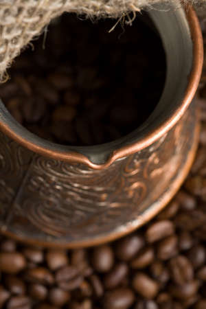 Cezve with freshly roasted coffee beans on sackcloth. Shallow depth of field. Focus on cezve throatの写真素材