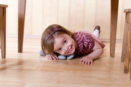 Happy little girl with toy on the hardwood floor crawling under tableの写真素材