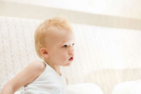 Pensive little boy sitting on white sofa at homeの写真素材