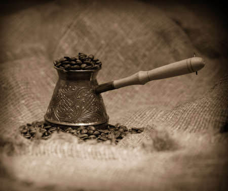 Sepia toned image of cezve with freshly roasted coffee beans on sackcloth. Image slightly vignetting on the corners for center accentingの写真素材