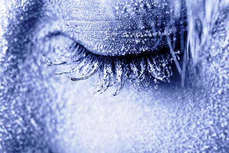 Frozen woman's eye covered in frost. Close-up shot toned in blueの写真素材