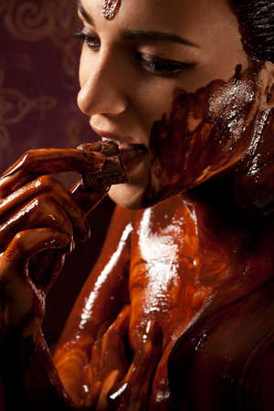 Woman covered in melted chocolate tastes chocolate bar and enjoyの写真素材