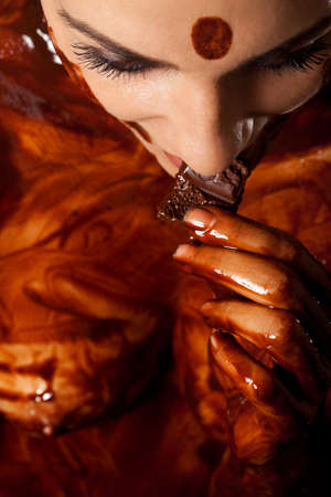 Woman covered in melted chocolate tastes chocolate bar and enjoyの写真素材