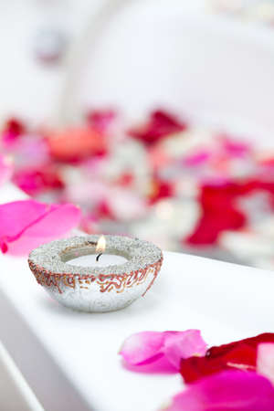 Spa treatment bathtub with candles and floating rose petals. Focus on candleの写真素材