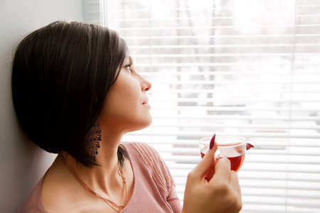 Brunette woman look at window and relaxing with cup of hot teaの写真素材