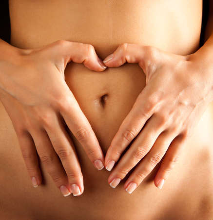 Woman touches tummy forming a heart shape with her fingers.の写真素材