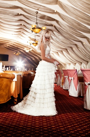 Beautiful blond girl in a wedding dress posing at restaurantの写真素材