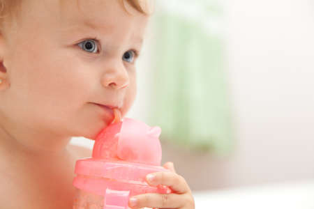 The little blue-eyed baby girl drinks juice from a bottle