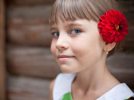 Attractive seven-year old girl with a red flower in her hair in front of a log wallの写真素材