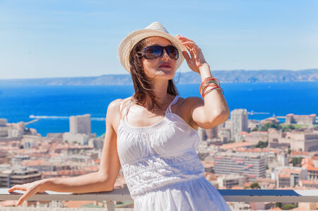 Happy traveling! Pretty girl in a hat and sunglasses posing against the city of Marseilleの写真素材