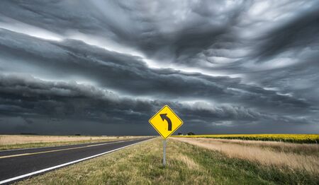Yellow and black curve road sign with stormy backgroundの写真素材