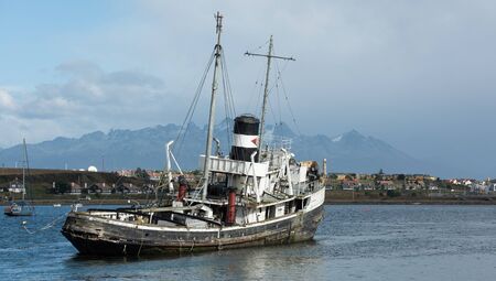 Ushuaia, Argentina - April 2 2019: An old British 2nd World War ship aground and a military neighborhood in the background.のeditorial素材