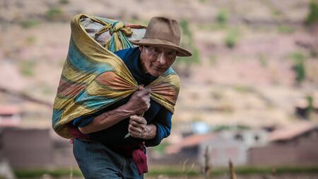 Pisac, Peru - August 12 2011: An old man carrying a heavy bag of cereals.のeditorial素材
