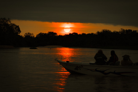 Sun setting over silhouetted boat on riverの写真素材