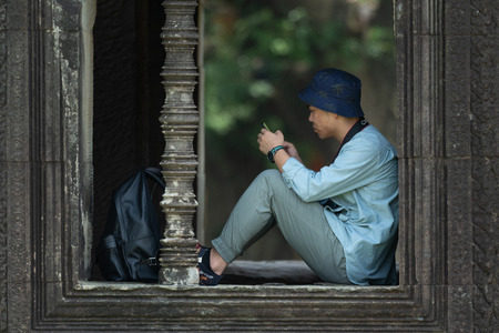 Tourist checks phone sitting in temple windowのeditorial素材