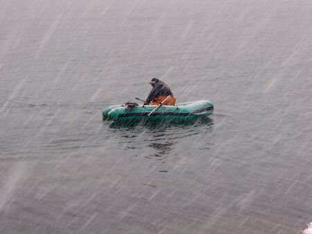 Ichthyologist on the inflatable boat recovers nets from the sea in heavy snowfallの写真素材
