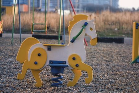 Swing horse toy for kids on a childrens playground. Swing for children on a kids playground. Yellow horse swing for kids. Children playground with a wooden horse swing.の写真素材