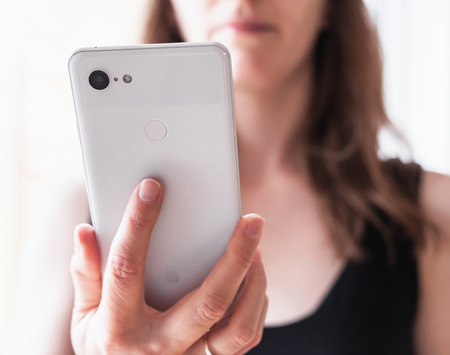 Woman holding Google Pixel 3 XL in front of plain background