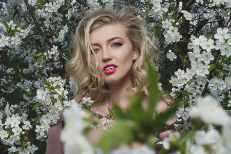 Beautiful sweet blue-eyed blonde girl in the garden near the cherry blossoms on a sunny bright day