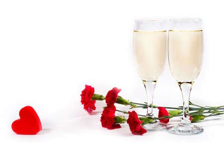 two glasses of champagne, carnation and red plastic heart on white background with copyspaceの写真素材