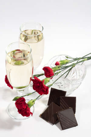 two glasses of champagne or white wine with crystal vase, carnation and chocolate tiles. White background with copyspaceの写真素材