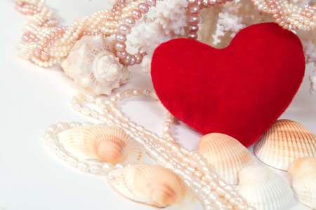 Red velvet heart with pearl beads, shells and corals on white background with copy space in the left-bottom cornerの写真素材