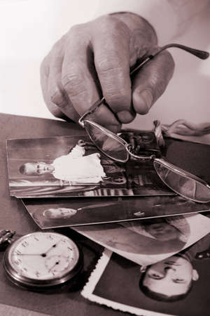 Old man's hands with glasses and some old portrets of this manの写真素材