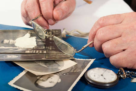 Old man's hands with glasses and some old portrets of this manの写真素材