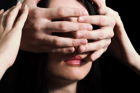 face of young pretty brunette woman closed by some man's hands, who stands behind herの写真素材