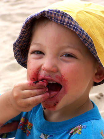 cute little boy siting on the sand and eating berriesの写真素材