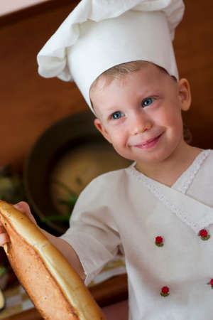 little boy in the cook costume at the kitchen sitting on the tableの写真素材