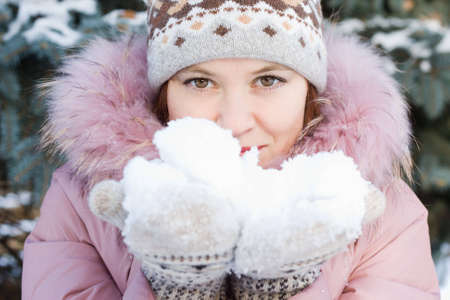Beautiful girl in hat and mittens holding some snowの写真素材