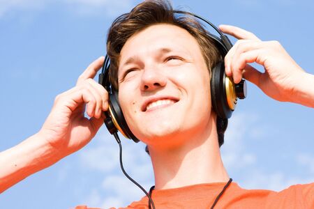 Young man listening for music on the blue sky background