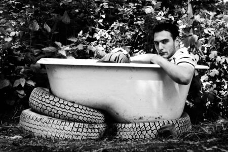 Black and white portrait of young adult man sitting in the bathtub outdoorsの写真素材