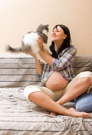 Young beautiful pregnant woman playing with her catの写真素材